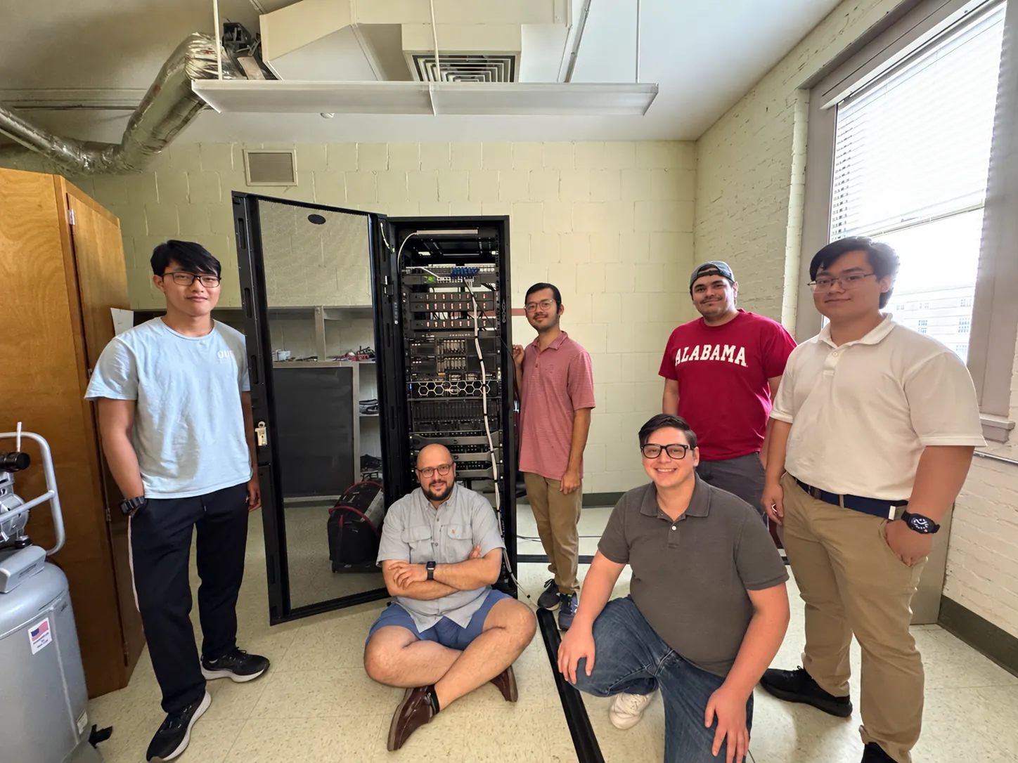 Six members of the group gathered around an open server rack of the computing cluster.