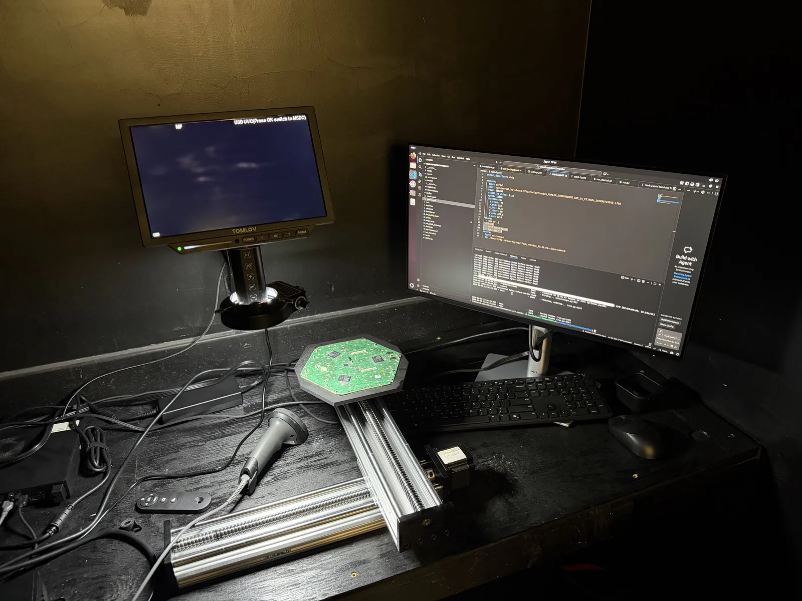 Visual-inspection station in a dark enclosure: a green hexaboard on a stage mounted on motorized rails, a microscope camera on a stand with its own display, and control software on a computer monitor.